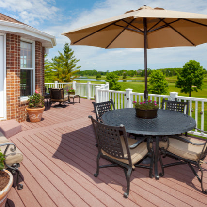 Deck & RailingsSpacious deck with wicker chairs and a round table under a large tan umbrella. Scenic view of trees and a green lawn under a partly cloudy sky.